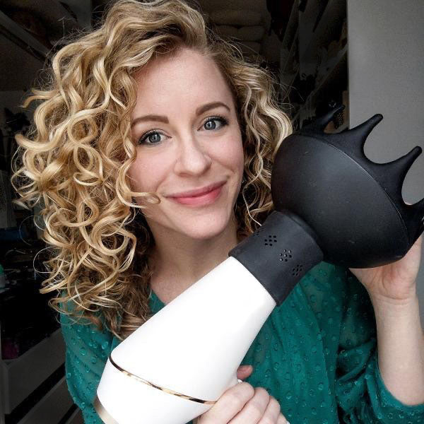 Smiling blonde curly hair woman holding a hair dryer with a SnozzlePro attached to an Xtava Black Orchid hair diffuser
