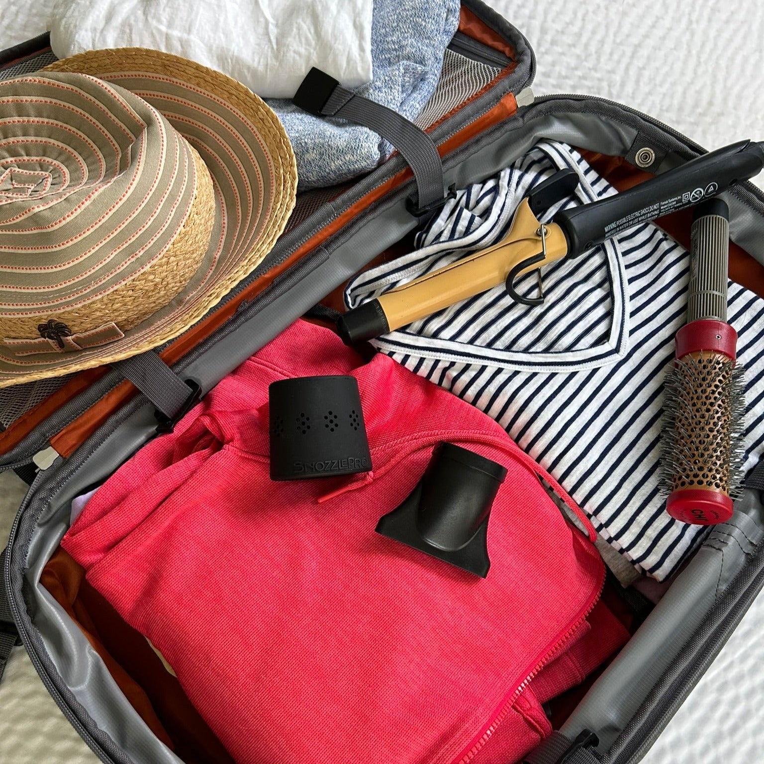 Suitcase packed for travel with SnozzlePro nozzle adapter and hair dryer concentrator nozzle