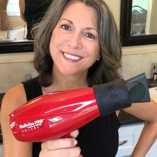 Smiling woman holding a red BabylissPro hair dryer with SnozzlePro concentrator nozzle attachment